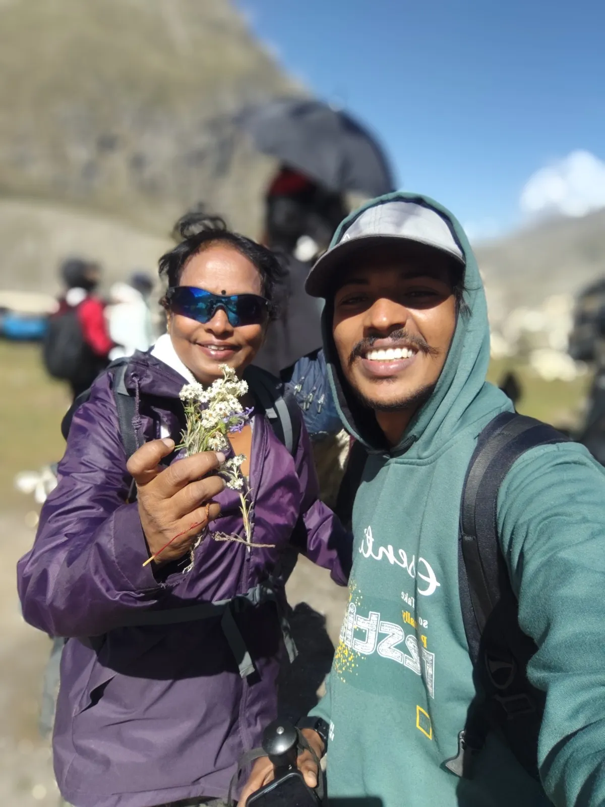 Roseleen holding a small bunch of white Himalayan wildflowers beside a smiling young fellow trekker at the end of the trek