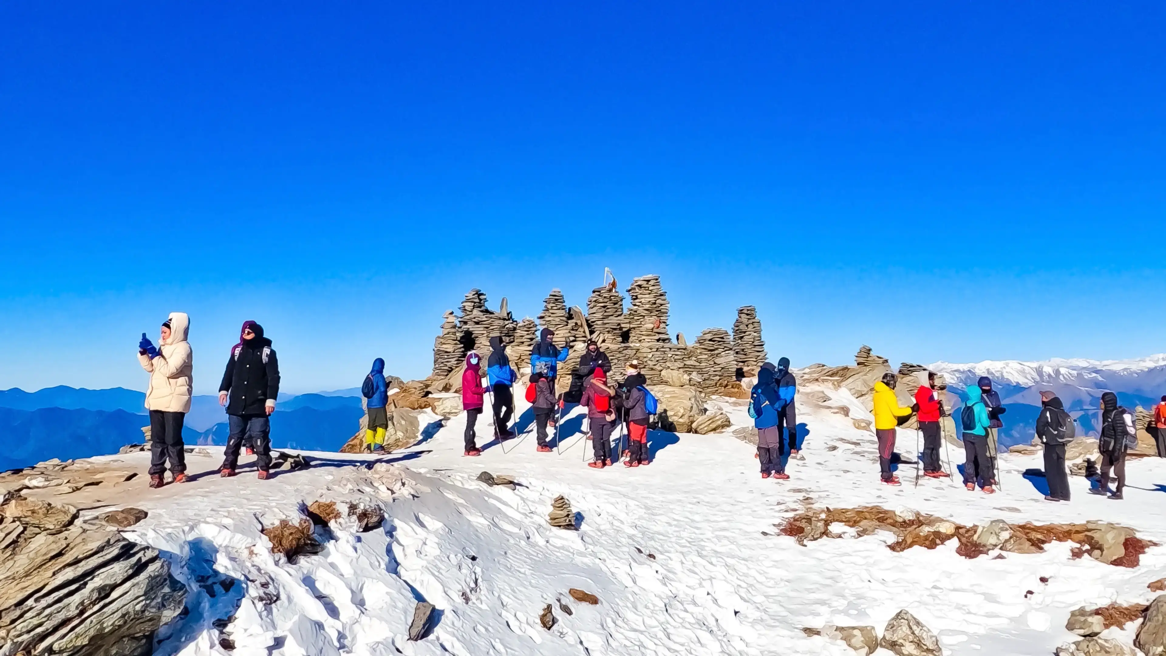 Trekkers at Kedarkantha summit with stone cairns and Himalayan views
